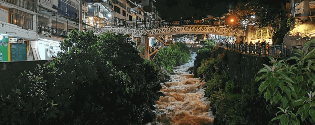 Ponte de pedestres iluminada sobre o rio no povoado de Aguas Calientes à noite, Machu Picchu, Peru