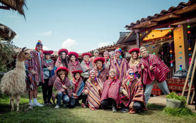 Turistas com ponchos tradicionais e uma lhama em uma hospedagem no Vale Sagrado de Cusco
