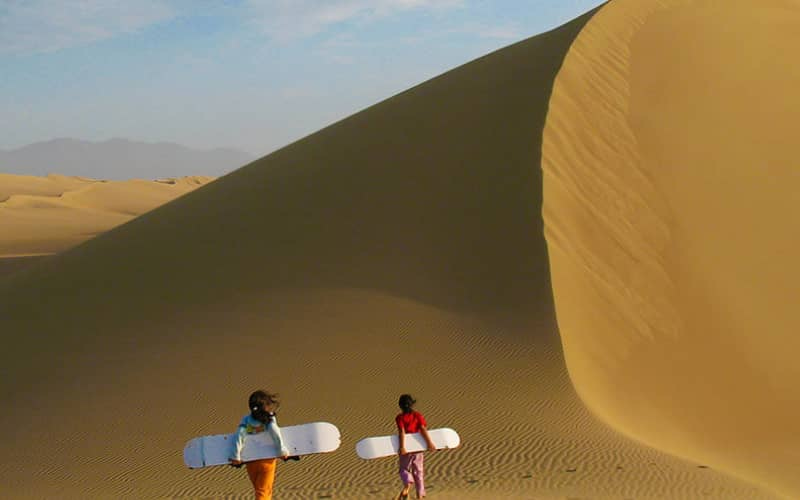 Turistas con tablas de sandboard en las Dunas de Usaka al atardecer, Nazca