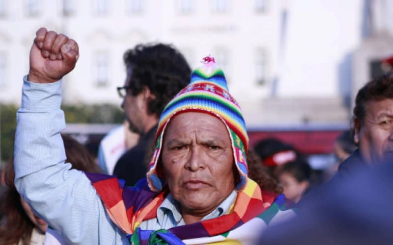 Andean man with a chullo and wiphala at a cultural celebration, part of Peru's customs