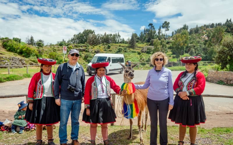 Tourists next to Andean women and a llama in Cusco, a cultural experience when traveling to Peru