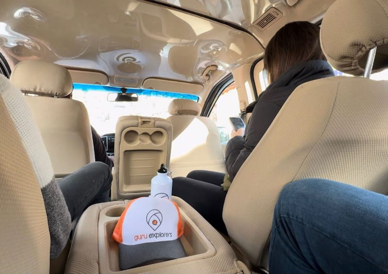 Interior de una van de transporte turístico privado de Guru Explorers con pasajeros y un gorro de la agencia