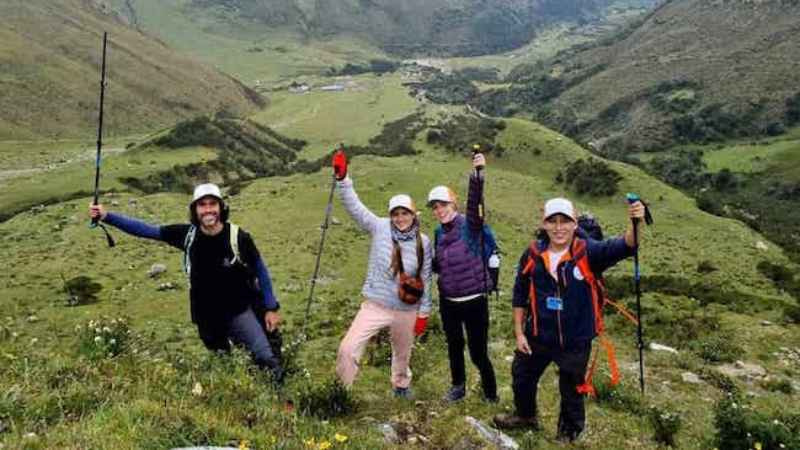 Grupo de senderistas con bastones de trekking y guia celebrando en el camino a la Laguna Humantay con el valle de Soraypampa al fondo