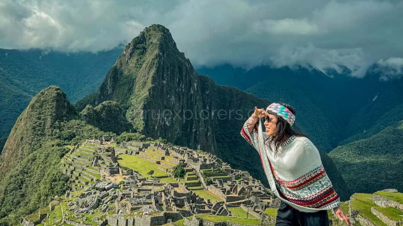Viajera con poncho andino contemplando las ruinas de Machu Picchu desde las alturas en el Camino del Inca