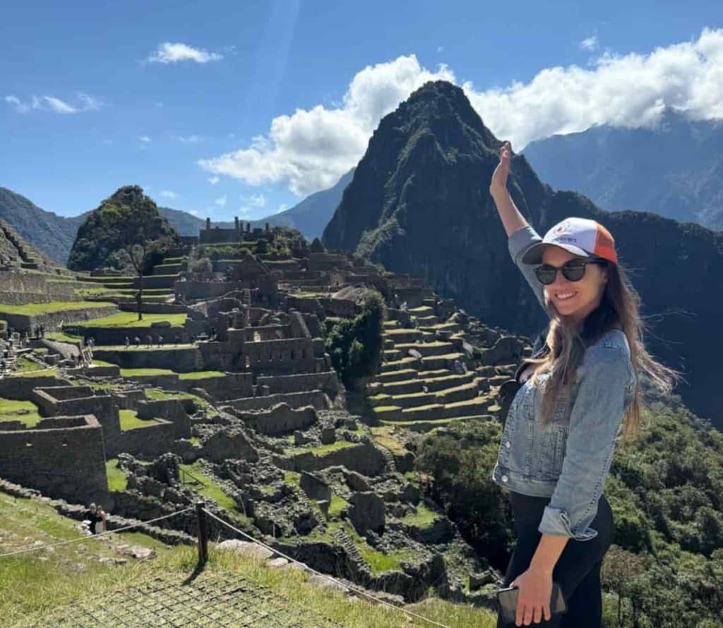 Turista levantando o braço em frente aos terraços de Machu Picchu e à montanha Huayna Picchu, em Cusco, Peru